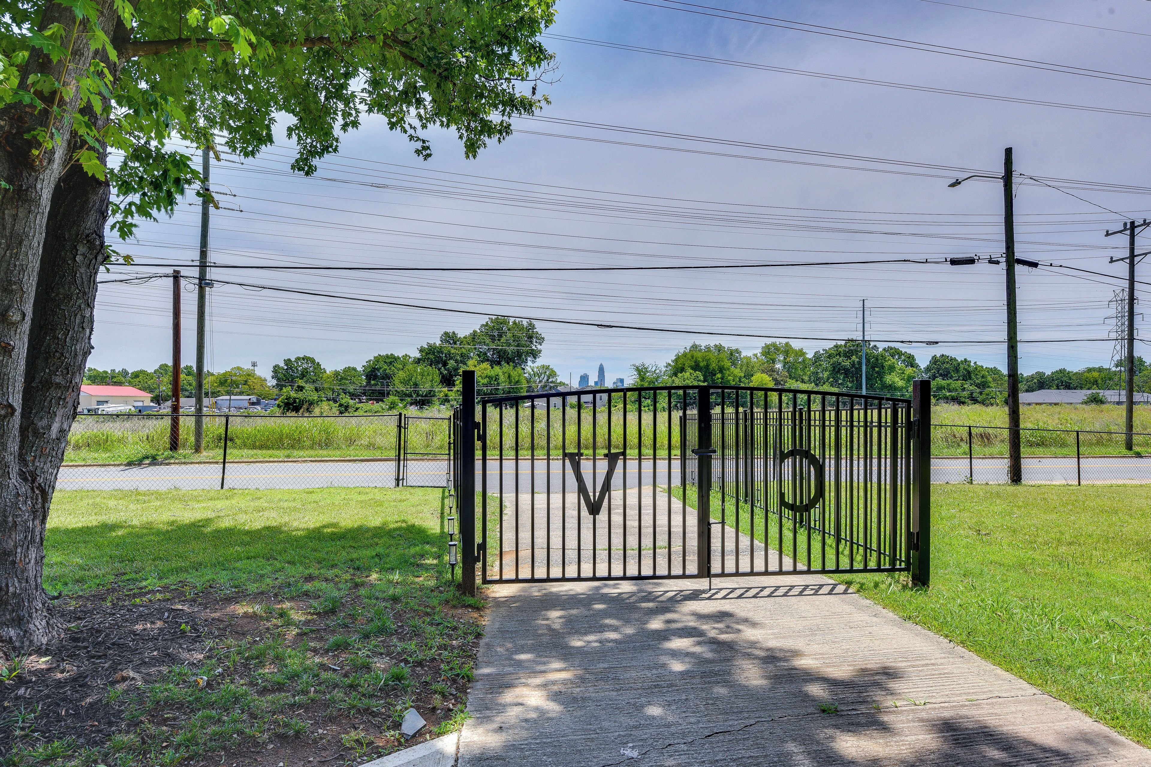 A gated entrance with a metal gate, a sidewalk, and a tree.