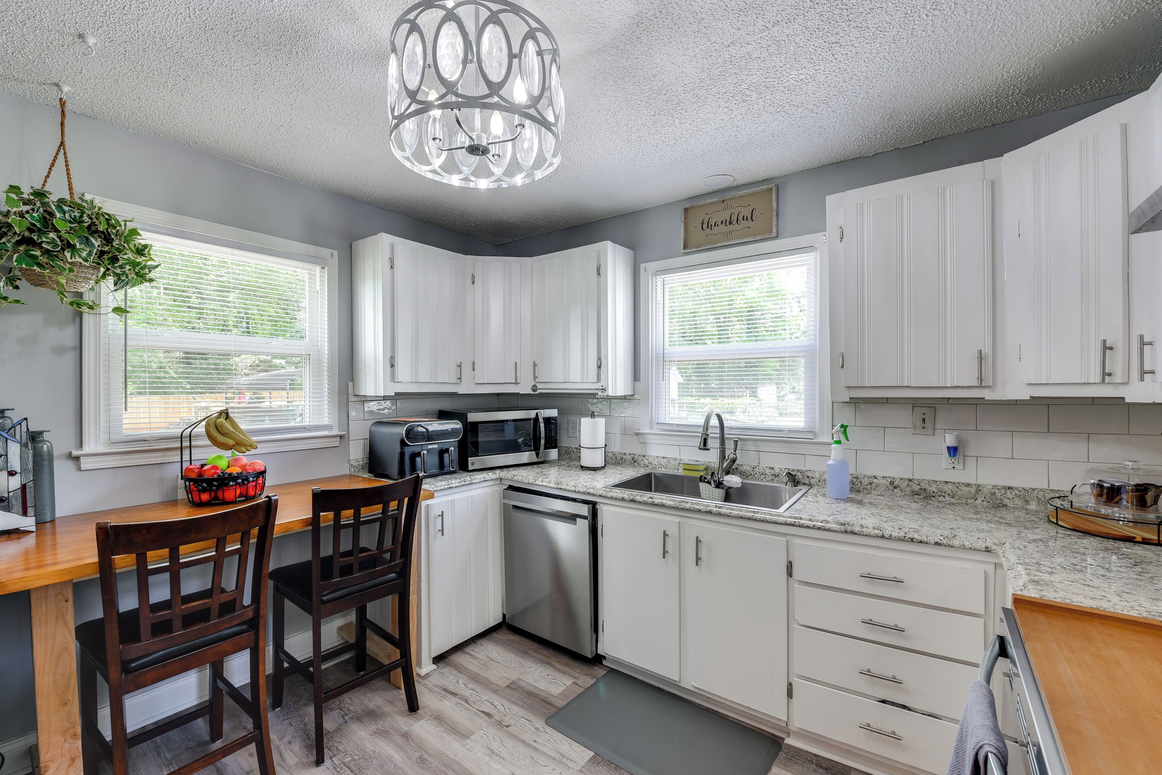 A modern kitchen with white cabinets, a wooden countertop, a built-in dishwasher, and a hanging plant.