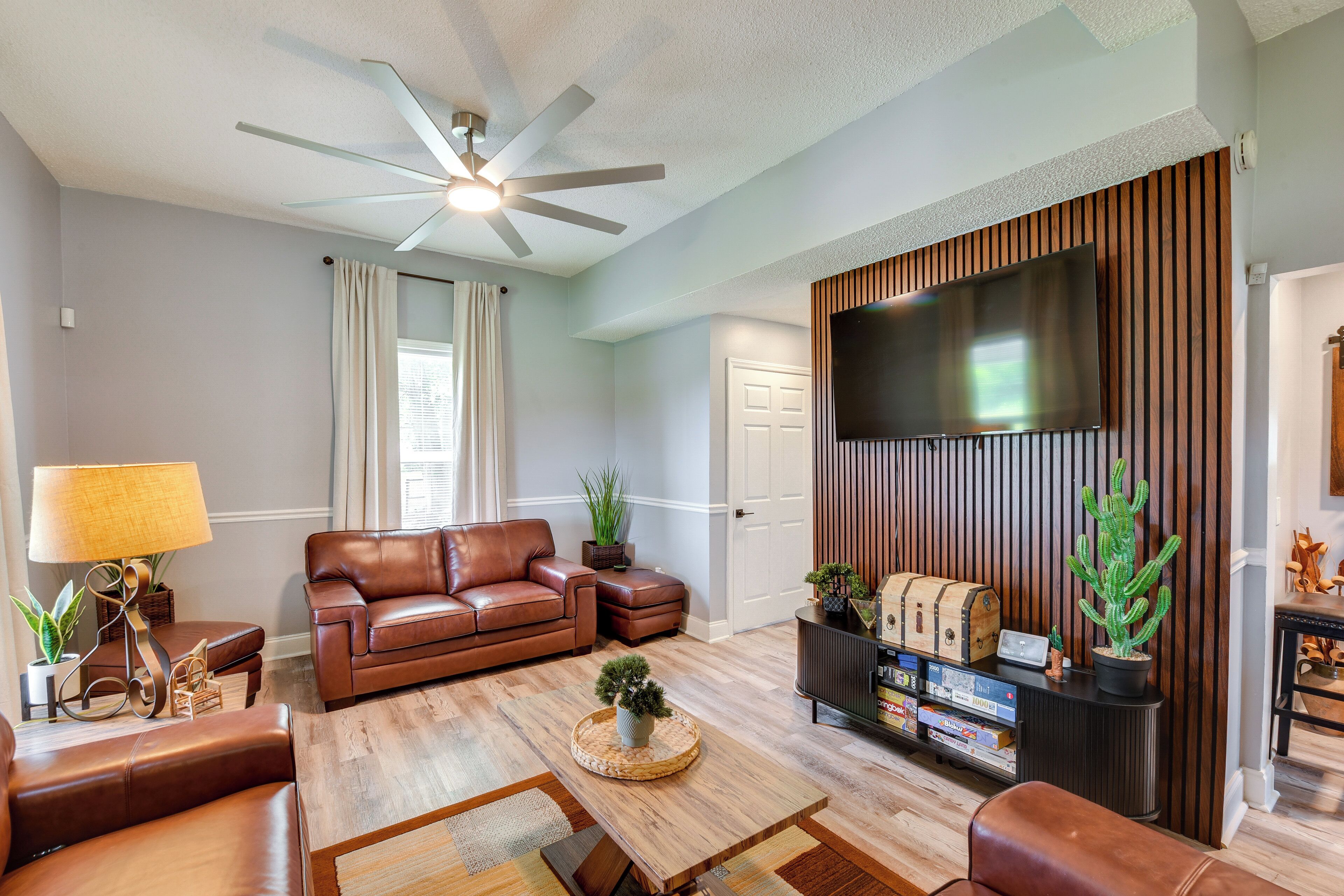 Un salon doté d’un ventilateur de plafond, d’un canapé en cuir, d’une table basse en bois et d’un téléviseur à écran plat fixé à un mur en bois.