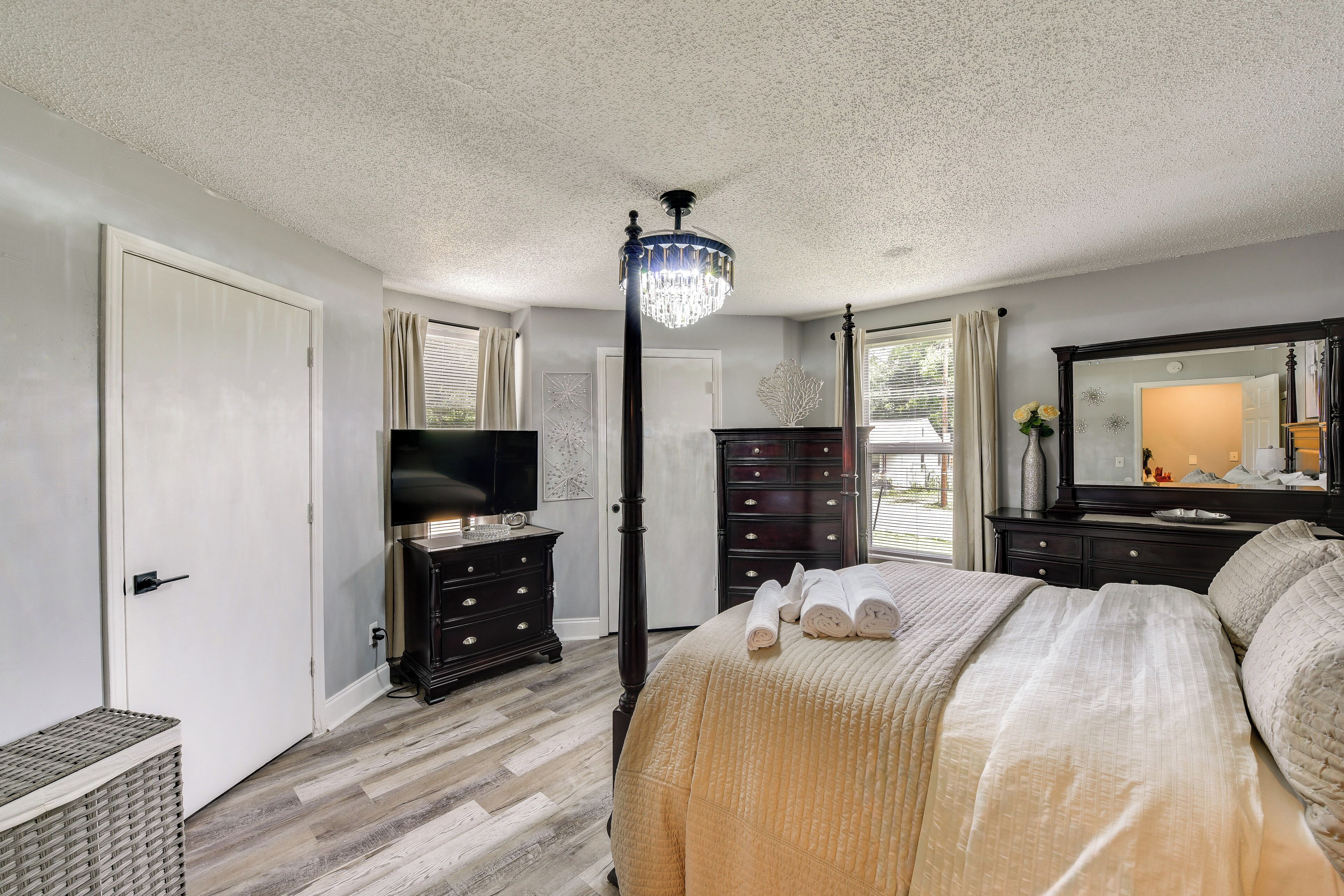 A bedroom with a four-poster bed, a television, a dresser, and a chandelier.