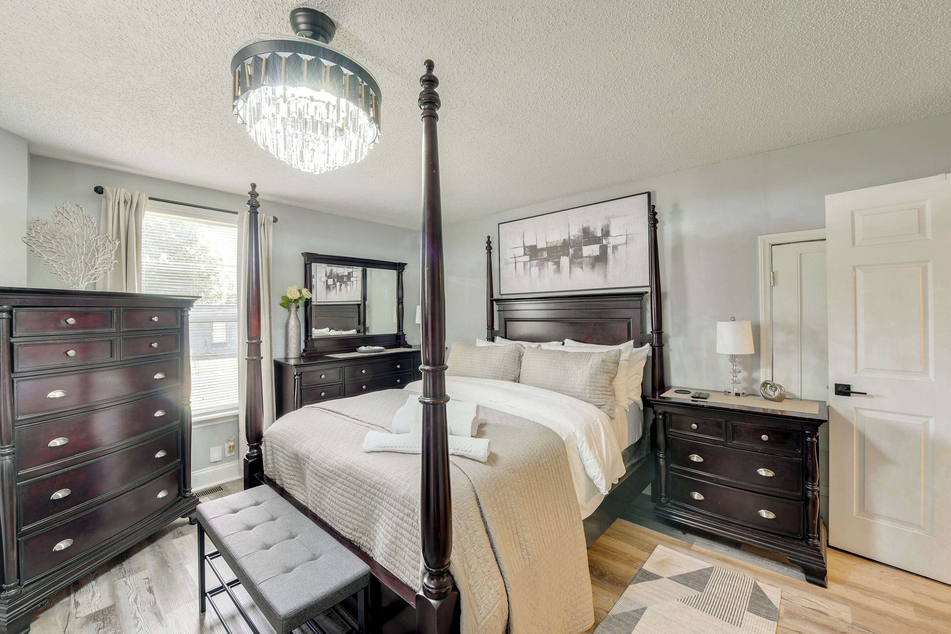 A four-poster bed with a canopy, dark wooden dresser, bedside tables, and a chandelier.