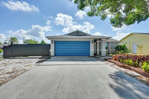 Eine Garage mit blauem Tor, einer Betonauffahrt und einem angelegten Garten mit tropischen Pflanzen.