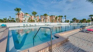 A swimming pool with lounge chairs, palm trees, and a building with balconies in the background. - Steps to Beach! Charming Indian Shores Condo (Indian Shores)