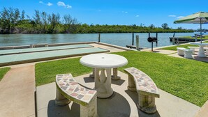 An outdoor patio with a table and benches, a grill, and a view of a lake. - Steps to Beach! Charming Indian Shores Condo (Indian Shores)