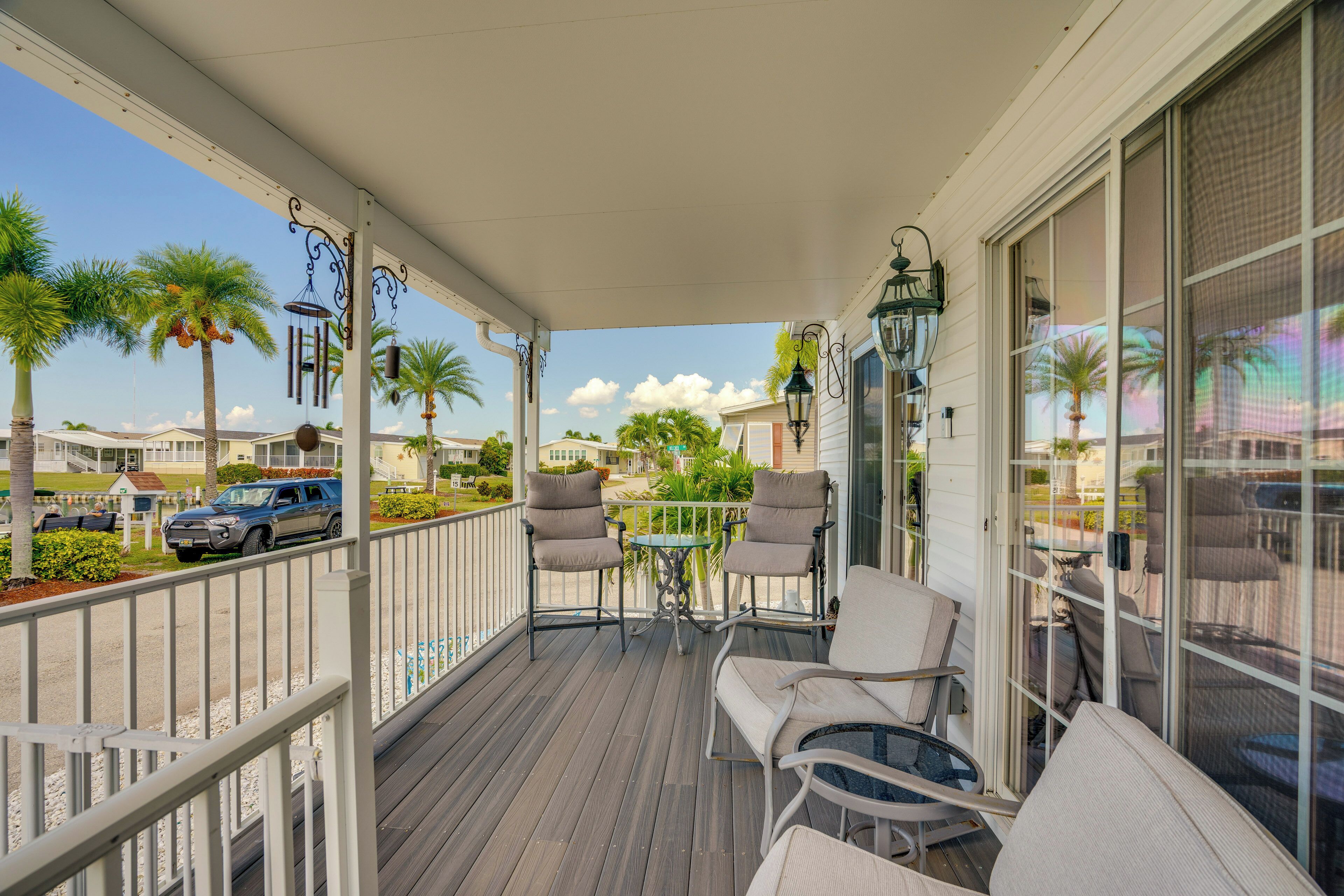 A covered outdoor area with a table and chairs, a pool, and a view of palm trees and houses.