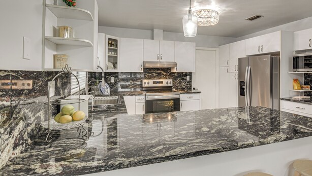 Una cocina moderna con armarios blancos, encimera de mármol y horno empotrado.