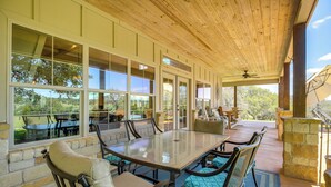 Um alpendre coberto com mesa e cadeiras, grandes janelas e vista para o exterior.