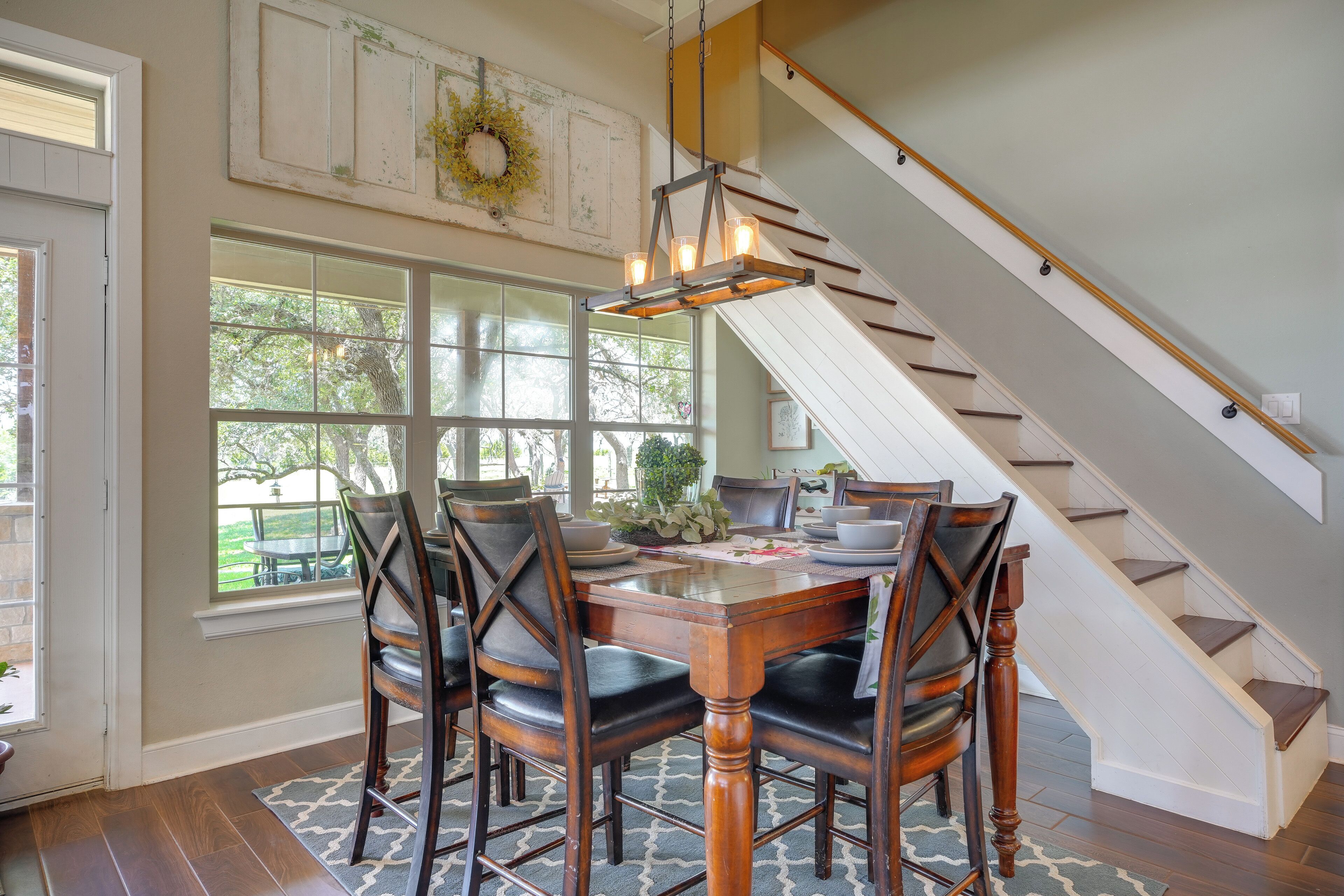 A dining area with a wooden table and chairs, a chandelier, and a staircase.