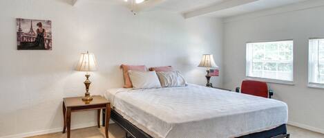 A bedroom with a bed, two bedside lamps, a ceiling fan, a rug, and a painting on the wall.