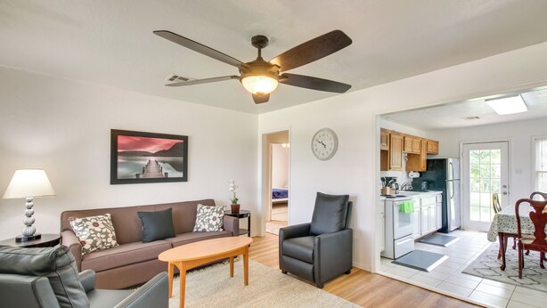 A living room with a sofa, a coffee table, a chair, a ceiling fan, and a kitchen area with cabinets and appliances. - 3 Mi to Fort Sill! Family Retreat w/ Fenced Yard (Lawton)