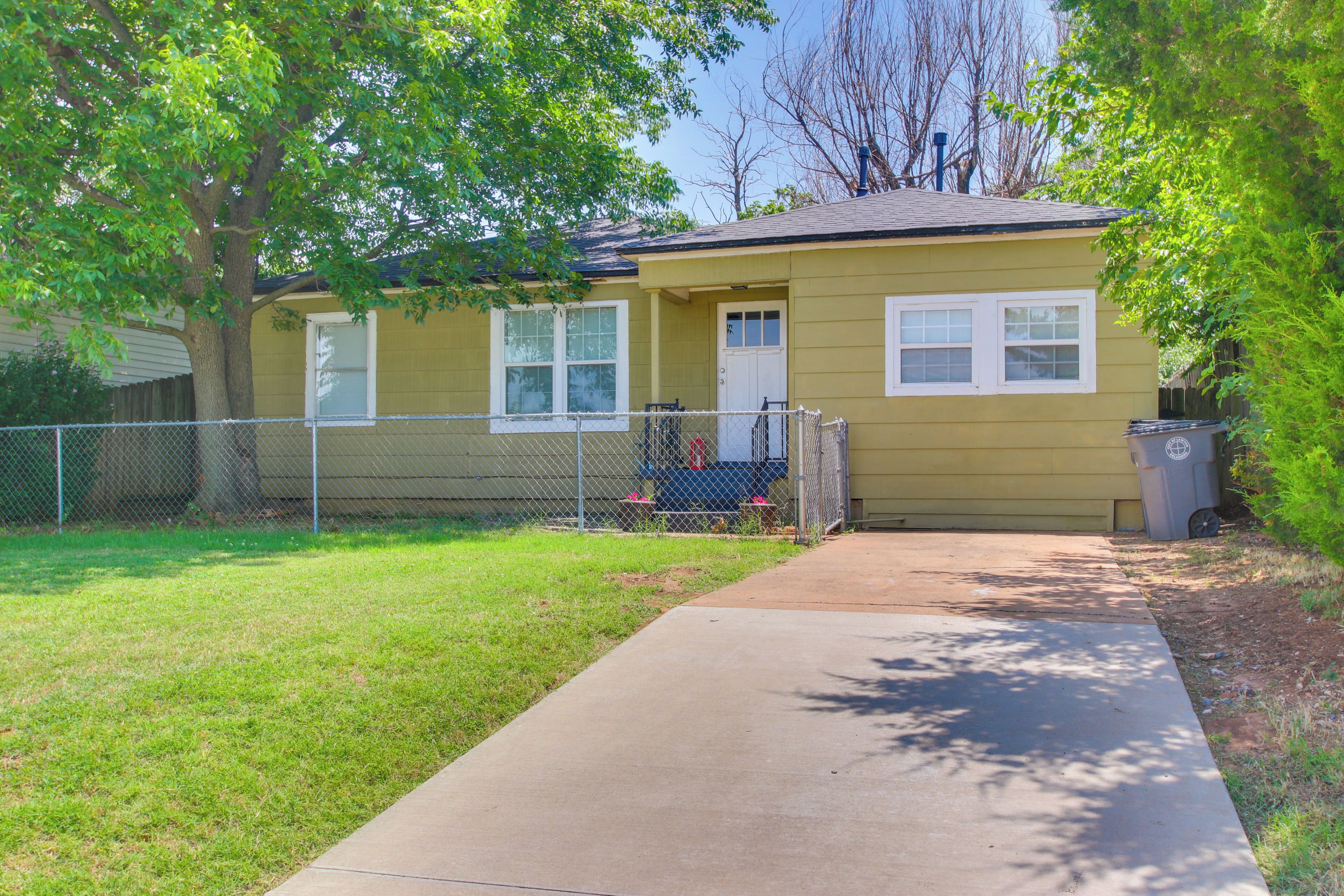 A single-story house with a front yard, a sidewalk leading to the front door, and a chain-link fence.