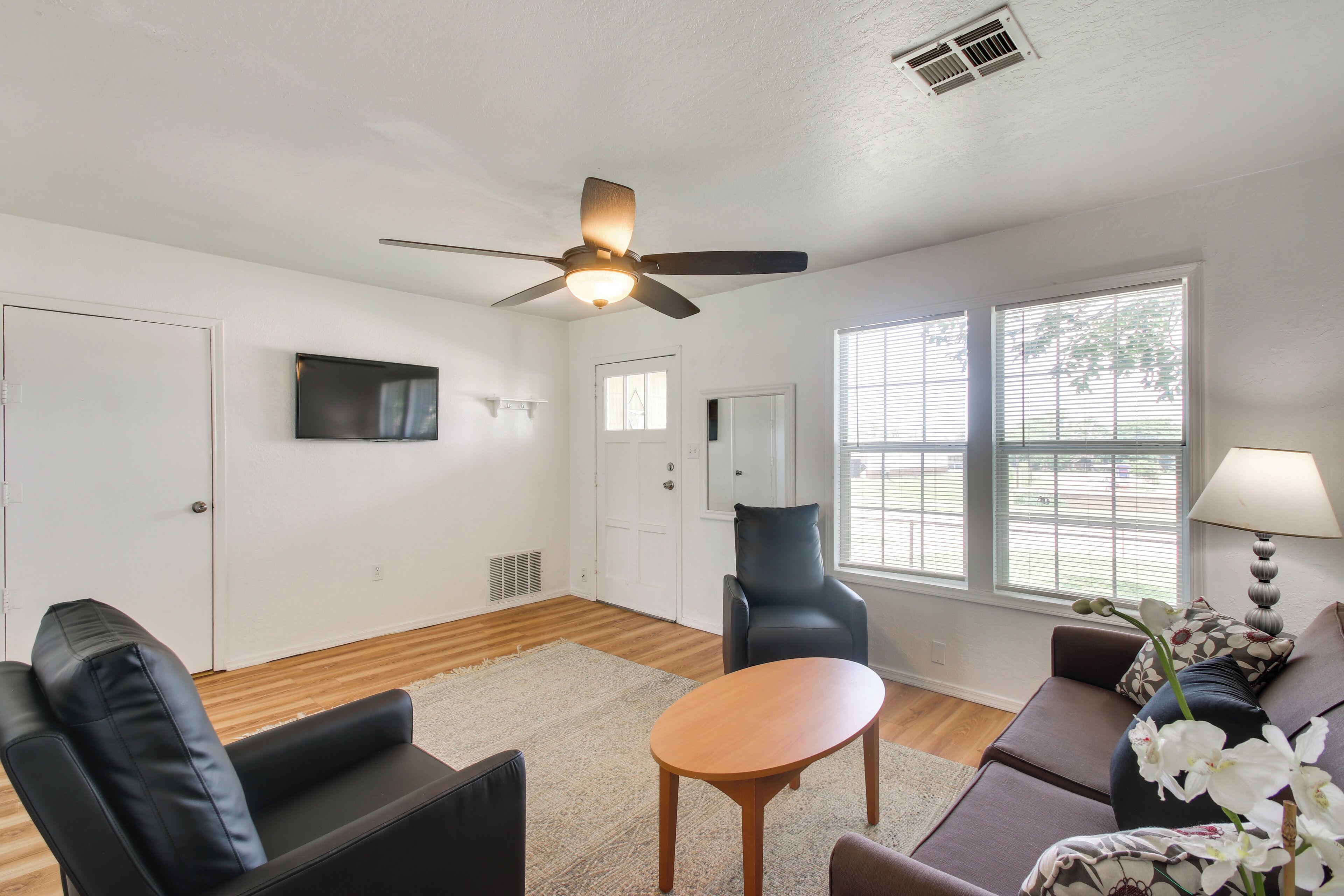 Una sala de estar con ventilador de techo, televisor de pantalla plana, sofá, sillón y mesa.