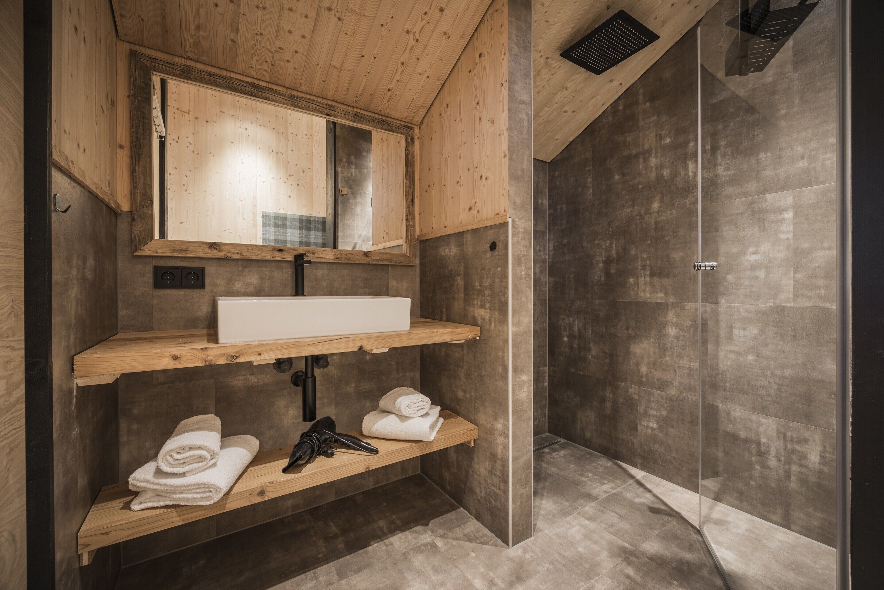 A modern bathroom with wooden shelves, a white sink, and a glass shower enclosure.