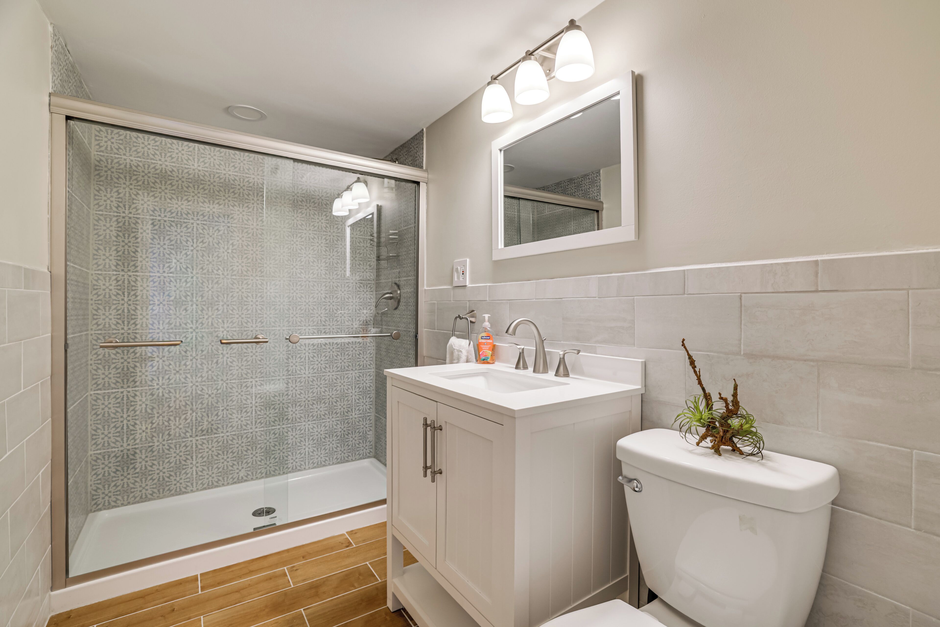 A bathroom with a shower, sink, toilet, and a mirror.