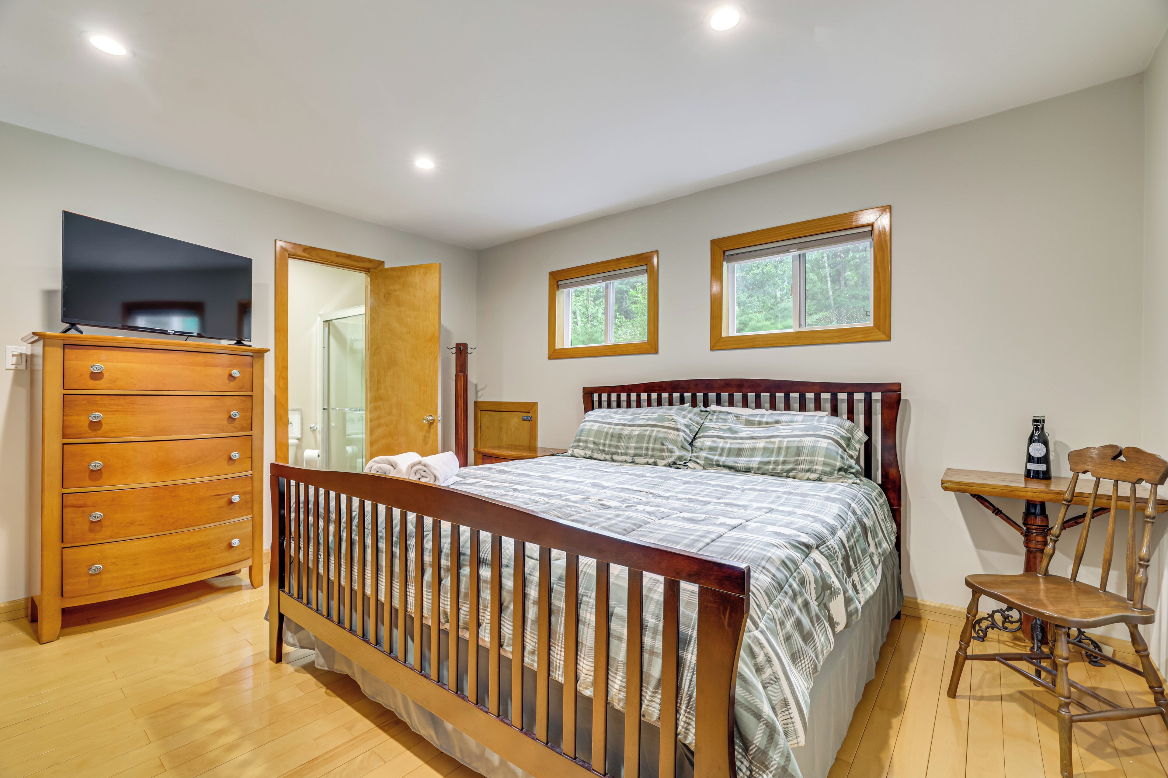 A bedroom with a wooden bed, a dresser, a chair, and two windows.