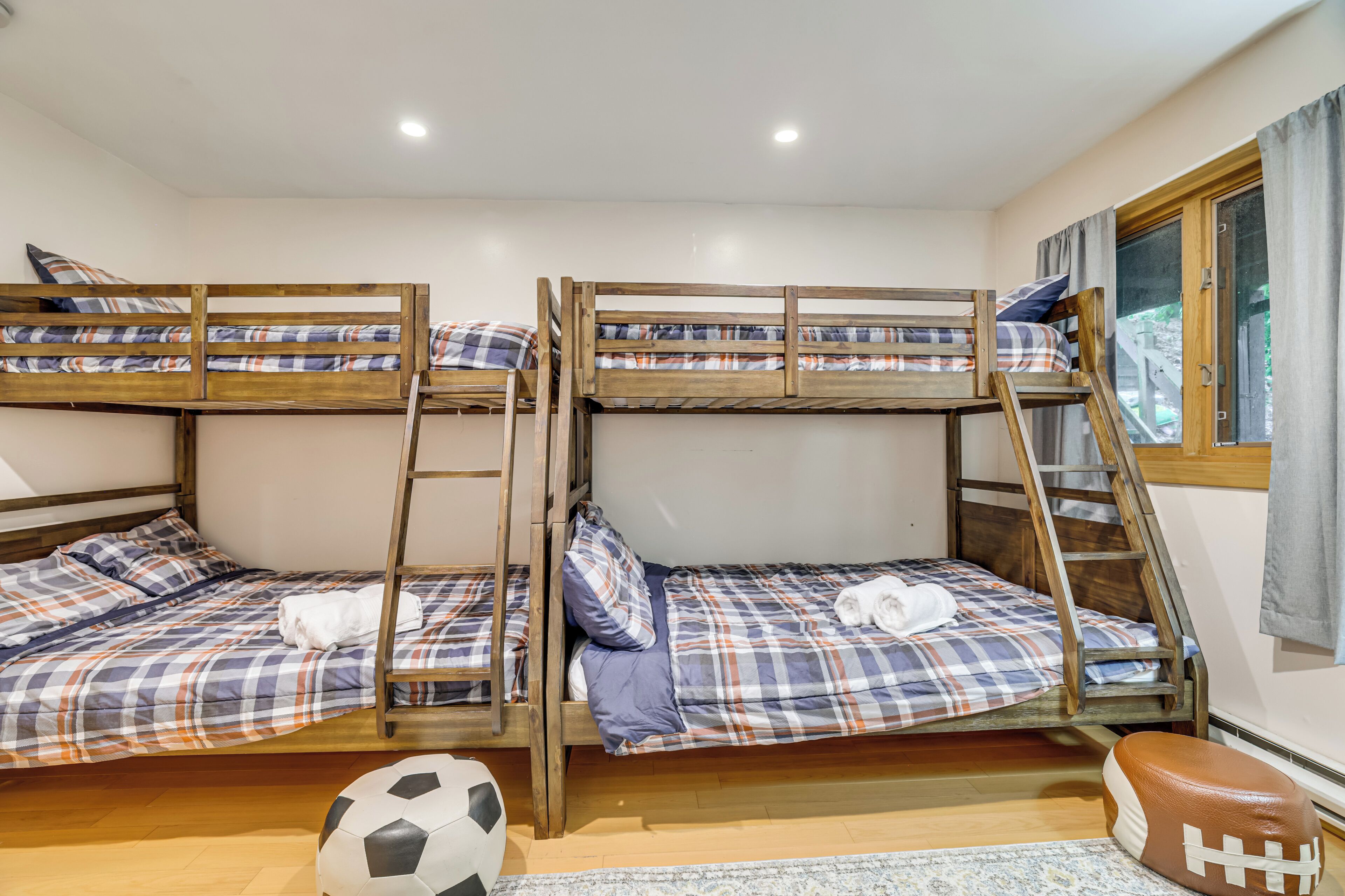 A room with three bunk beds, a soccer ball, a football, and a window with curtains.