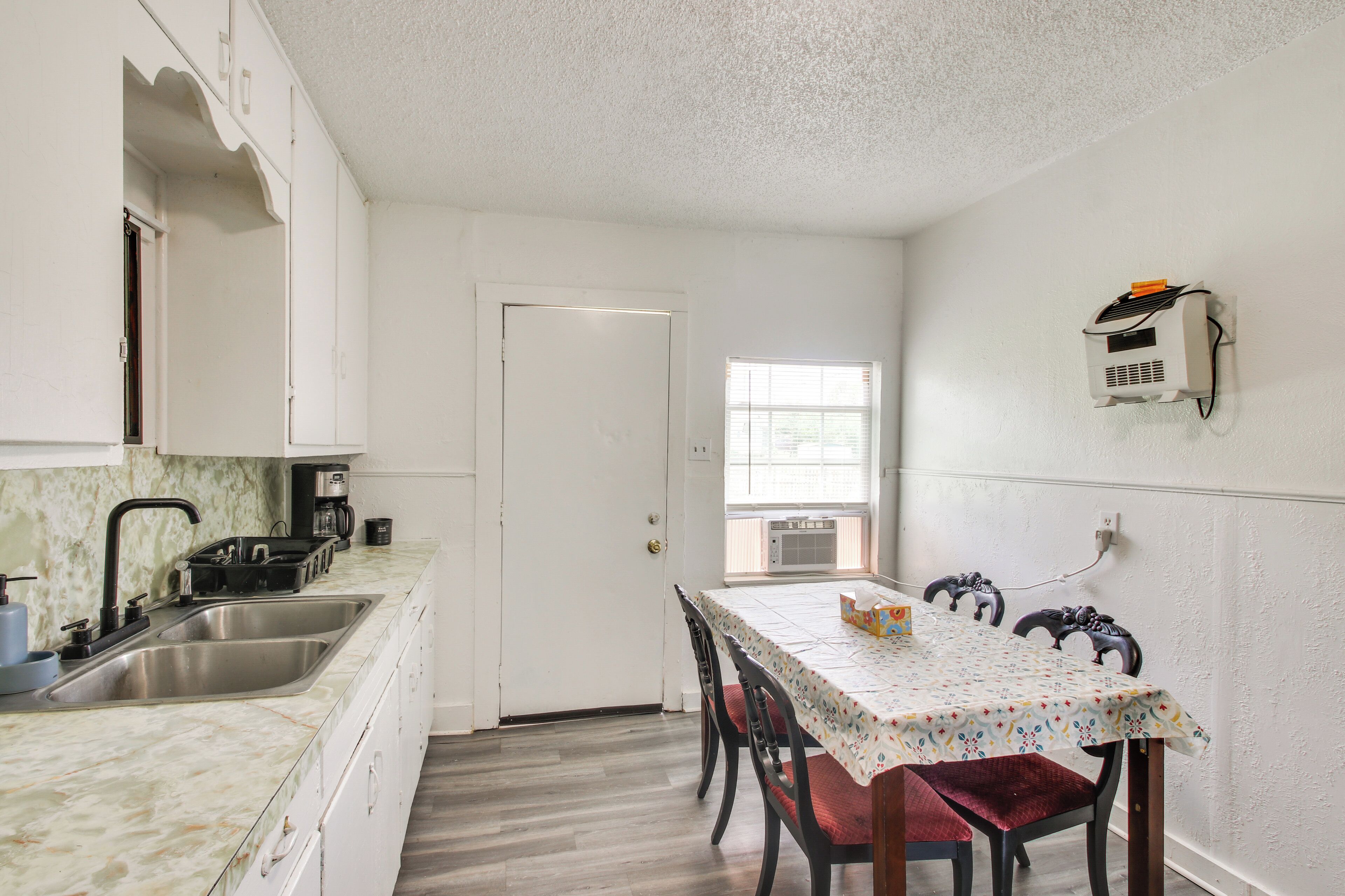 A kitchen with a sink, stove, and coffee maker, a dining table with chairs, and a window with blinds.