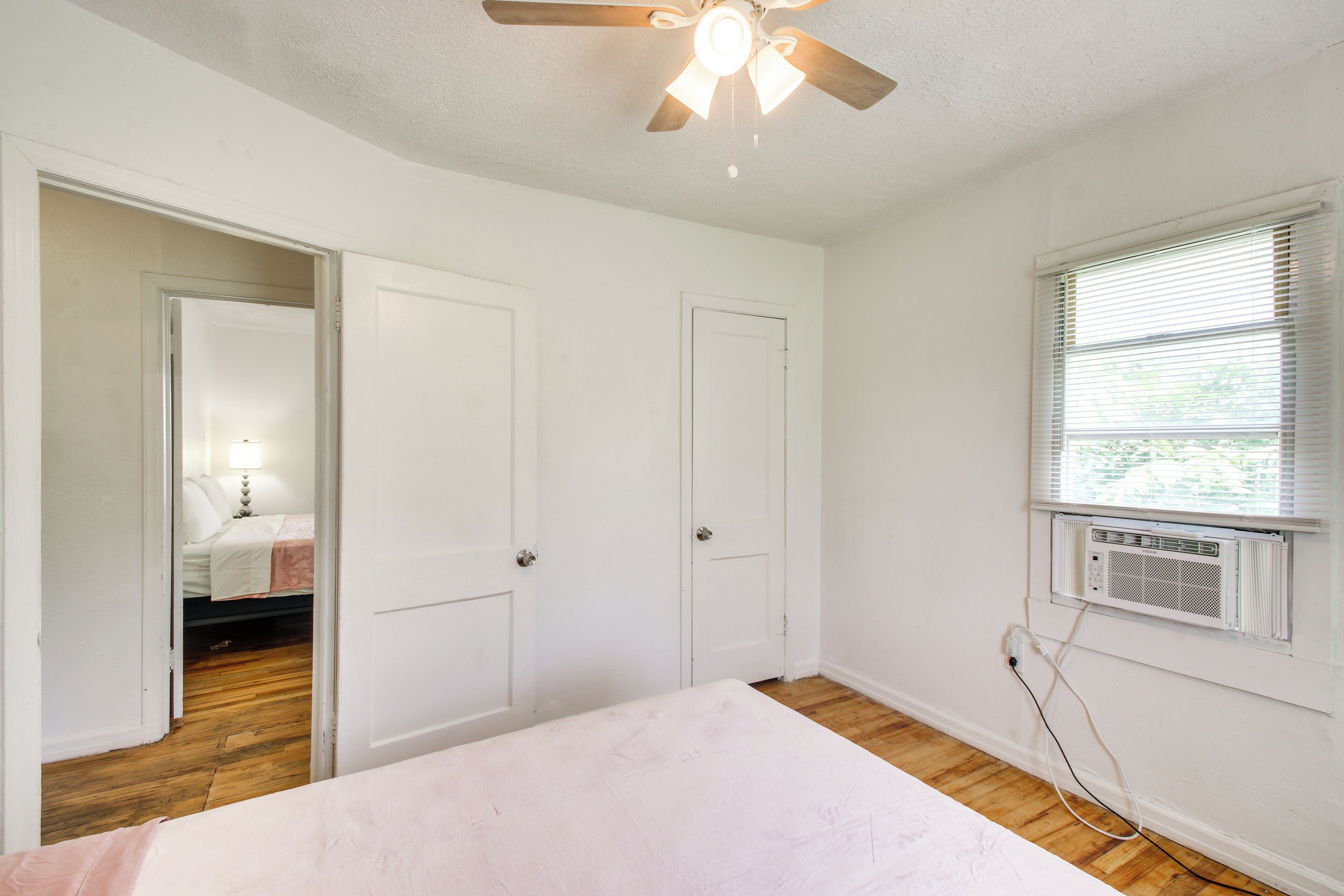 Une chambre à coucher comprenant un lit, deux portes, un ventilateur de plafond, un appareil de climatisation et une fenêtre.