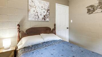 Een slaapkamer met een houten hoofdbord, een bed met een blauw beddegoed met een patroon, een witte deur en een bloemig kunstwerk aan de muur.