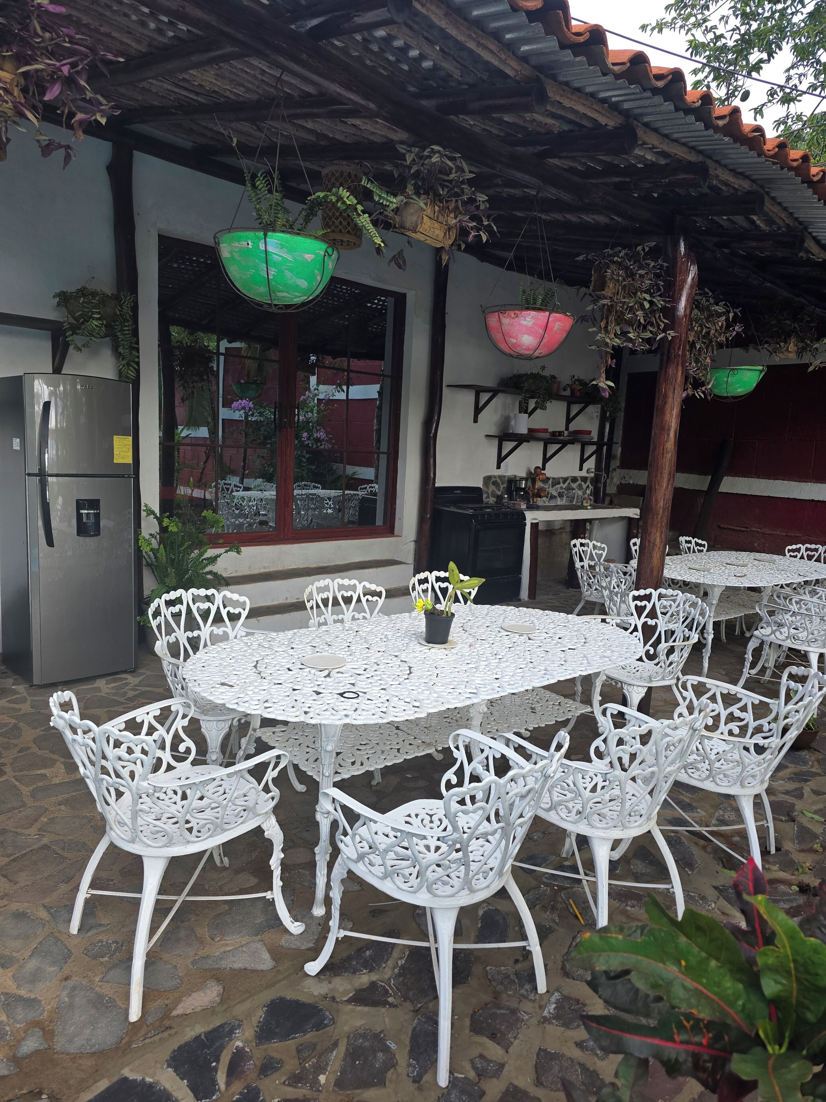 A patio with a round table and white chairs, a refrigerator, and hanging planters.