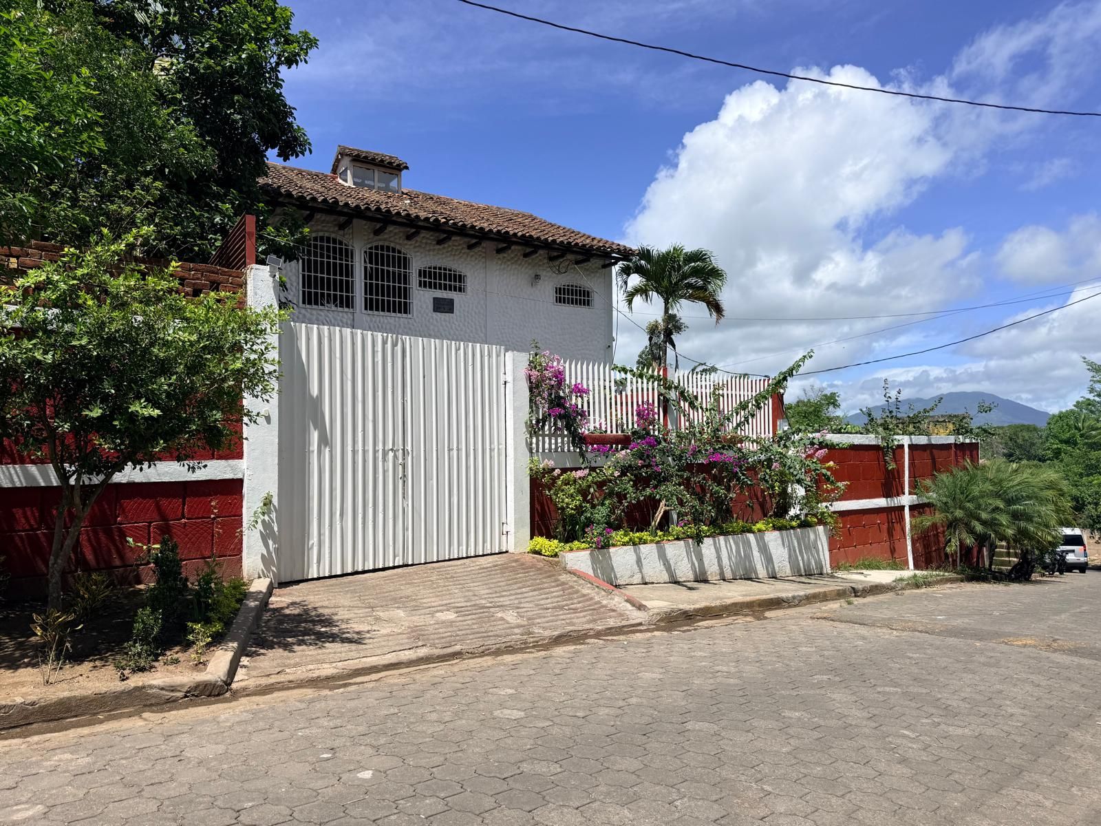 A residential house with a gated entrance, a tiled roof, and a paved driveway.