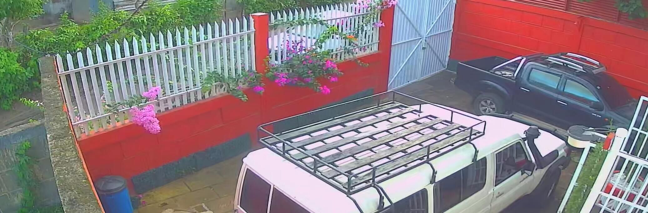 Un vehículo estacionado en un área roja con una valla blanca y flores.