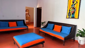 A room with two sofas and a bed, a painting on the wall, and a potted plant.