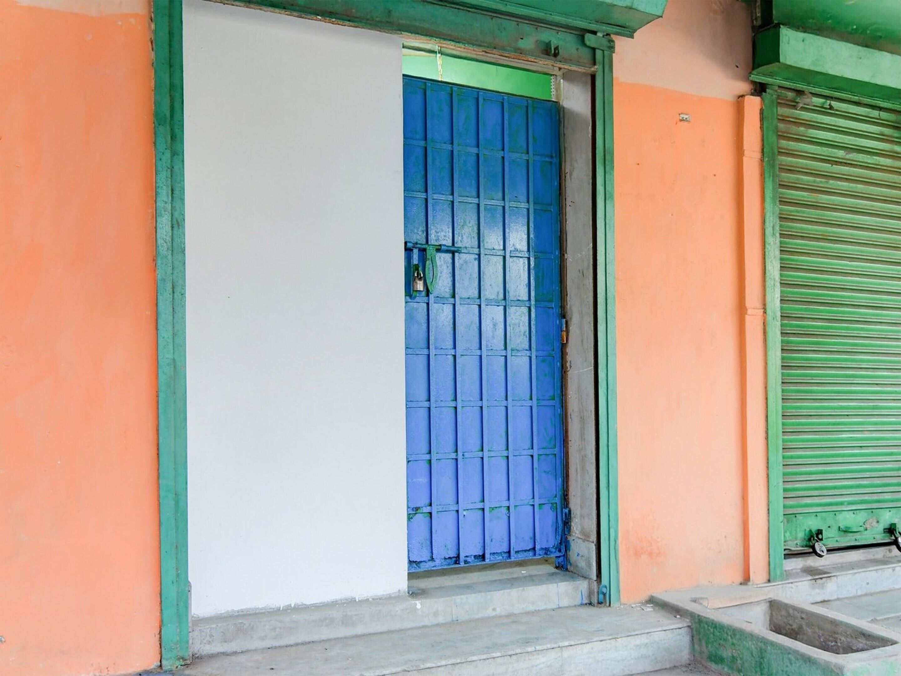 A building entrance with a blue door, green trim, and a closed green shutter.