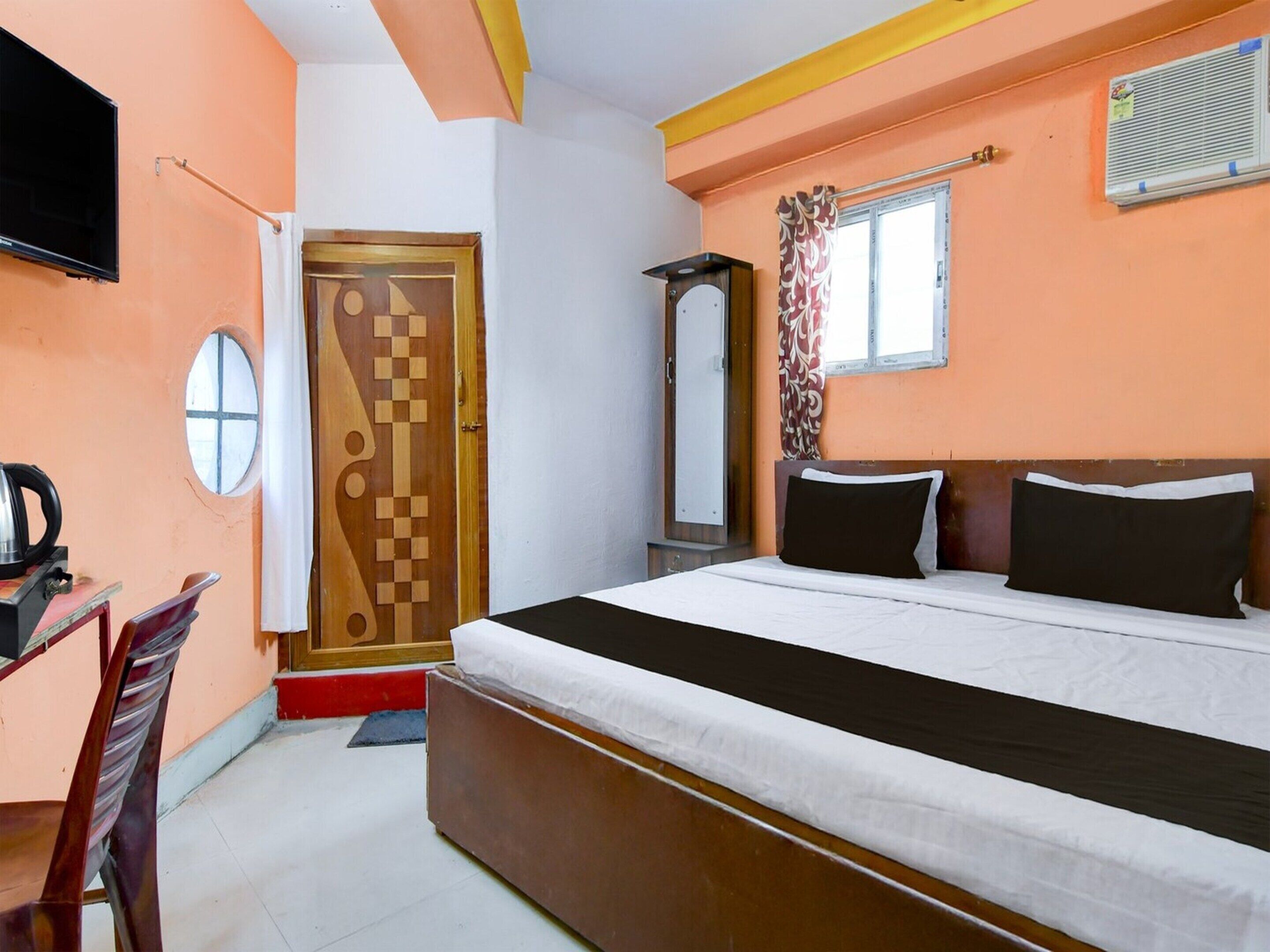 A bedroom with a bed, a TV, a mirror, a window with curtains, and a door with a geometric design.