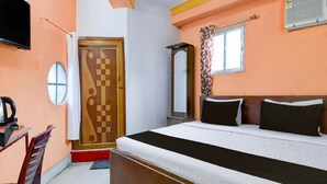 A bedroom with a bed, a TV, a mirror, a window with curtains, and a door with a geometric design. - Classic Hotel Ameesha Lodge (Barakpur)