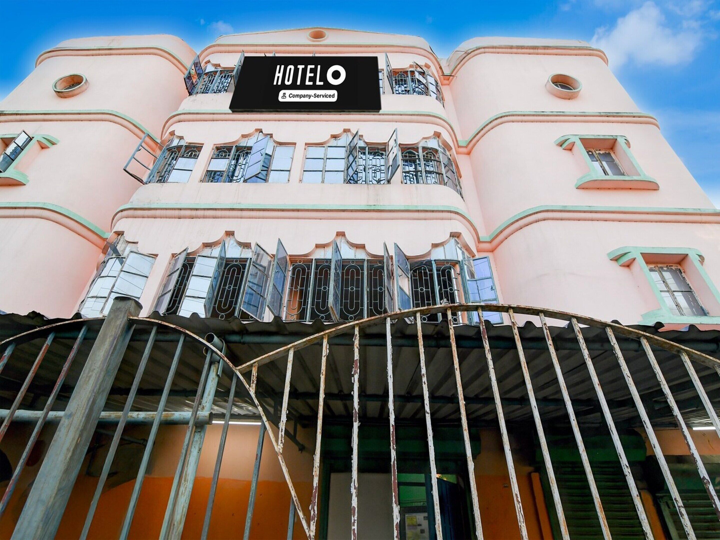 A pink building with a sign reading 'HOTELO Company Serviced' and a gated entrance.