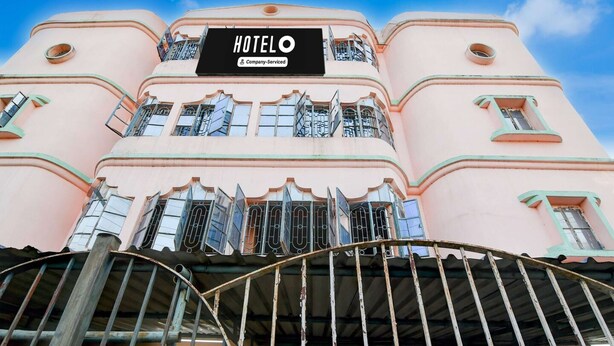 A pink building with a sign reading 'HOTELO Company-Serviced' and a metal gate in the foreground. - Classic Hotel Ameesha Lodge (Barakpur)