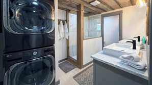 A modern bathroom with a built-in washer and dryer, a marble sink, and a wooden ceiling.