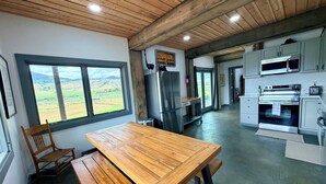 A modern kitchen with wooden beams, a large window with a view, stainless steel appliances, and a wooden dining table.