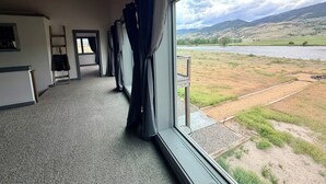 A room with a large window, a ladder, and a view of a lake and hills.