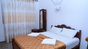 Un lit bien fait, recouvert d’une couvre-lit à motifs, une table de chevet avec une lampe et un miroir accroché au mur.
