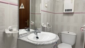 Un baño con lavamanos, espejo, inodoro y toallero.