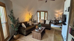 Una sala de estar con sofá, una mesa de centro y un ventilador de techo. Hay un comedor con mesa y sillas.