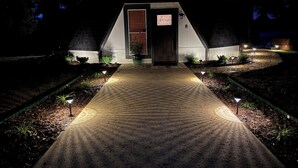 Un edificio con forma de cúpula, con una puerta central, rodeado de un jardín ajardinado con senderos y pequeñas luces.