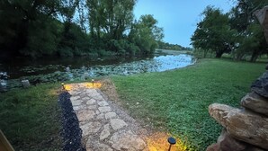 Un sendero de piedra que conduce a una masa de agua, rodeado de follaje y construcciones de piedra.