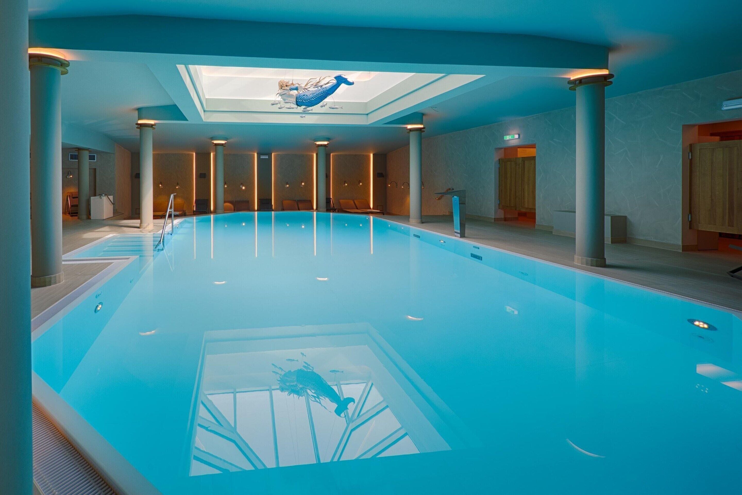 A large indoor swimming pool with a skylight, columns, and wooden doors.