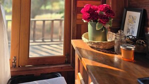 A wooden cabin interior with a window, a table with a vase of flowers, a framed picture, and a cup.