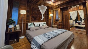 A wooden room with a bed, bedside table, lamp, and a window with curtains.
