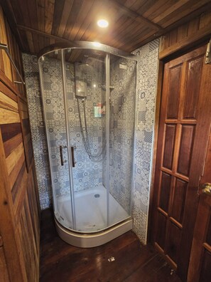 A shower enclosure with patterned tiles, a wooden door, and a ceiling light. - three little birds  2 bedroom  (Kanchanaburi)