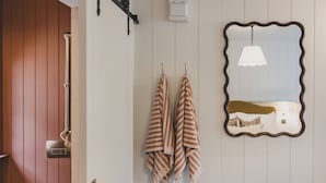 A bathroom with wooden paneling, striped towels, a mirror with a wavy frame, and a hanging light fixture.