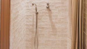 A shower with a handheld showerhead and a fixed showerhead, both mounted on a tiled wall.