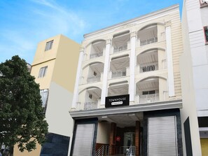 A multi-story townhouse with a balcony on the ground floor, a sign indicating it is a company-serviced property, and a closed shutter on the right side. - Deluxe Devi Residency (Hyderabad)