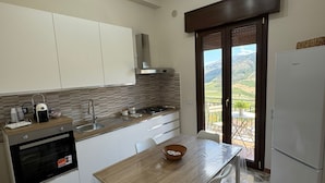 A modern kitchen with a wooden table, white cabinets, a built-in oven, and a view through a glass door to an outdoor area.