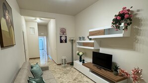A living room with a sofa, TV, decorative shelves, and a stone floor.