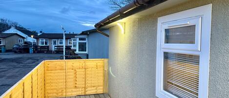 A wooden deck with a window and a light fixture on the house exterior.